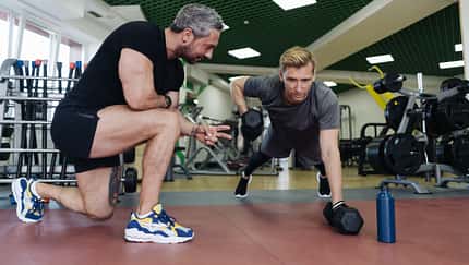 Mann trainiert mit einem Fitnesstrainer Ruderzüge im Stütz mit Kurzhanteln-
