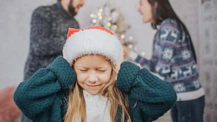 Ein Mädchen mit Weihnachtsmütze hält sich die Ohren zu, im Hintergrund sieht man, wie sich die Eltern lautstark streiten