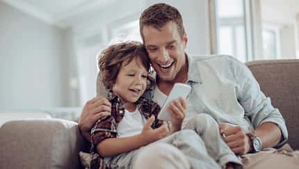 Vater und Sohn sitzen auf dem Sofa und amüsieren sich mit einem Smartphone