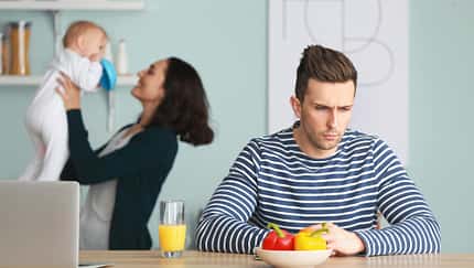 Im Hintergrund sieht man eine glückliche Mutter mit ihrem Säugling spielen, vorne sitzt der dazugehörige Vater und schaut bedrückt