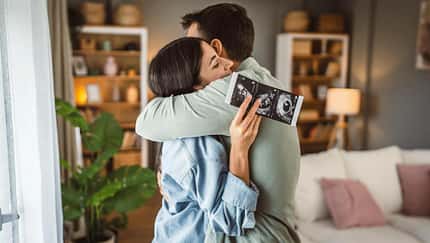Eine Frau und ein Mann umarmen sich, sie hält ein Ultraschallbild in der Hand