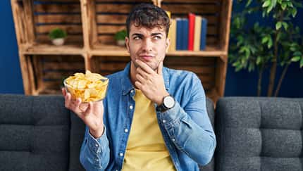 Mann guckt skeptisch auf Schüssel mit Chips