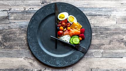 verschiedenes gesundes Essen auf einem runden Teller mit Besteck als Uhrzeiger