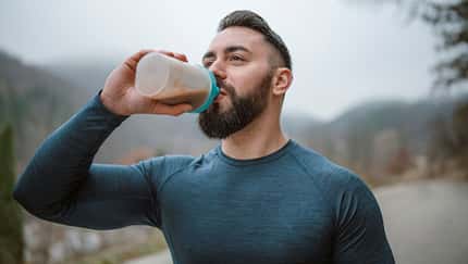 Ein junger Sportler trinkt draußen einen Protein-Shake