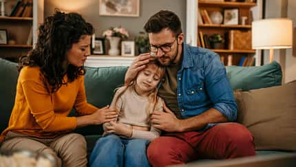 Mutter und Vater sitzen auf dem Sofa und trösten ihre traurige Tochter