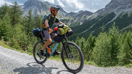 Man bikepacking, he cycles through the mountains and pine tree forests