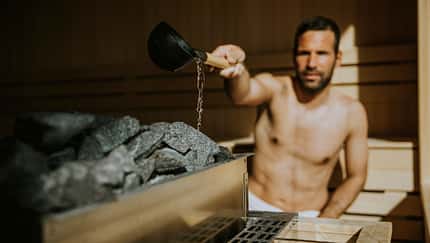 Junger Mann, der in der Sauna Wasser auf heißen Stein gießt