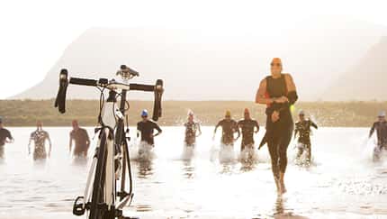 Triathleten laufen durch das Wasser zu ihren Fahrrädern