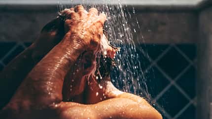 Engrossed in his grooming ritual, a man rinses his hair, the water's embrace enhancing the meditative quality of his daily routine.