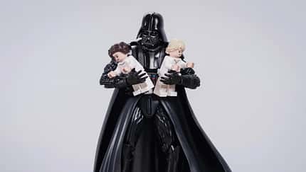 Darth Vader hält zwei übergroße Legofiguren von Leia und Luke im Arm