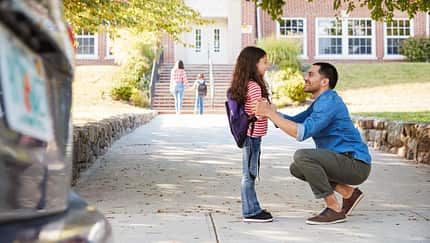 Ein Vater verabschiedet seine kleine Tochter vor der Schule
