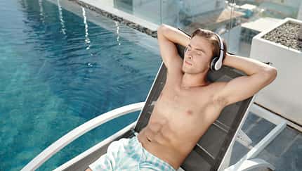 Junger Mann genießt ein Hörbuch am Pool