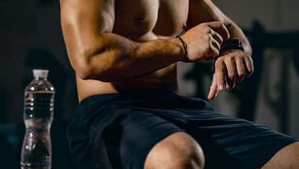 Beschnittenes Porträt eines jungen sportlichen Mannes, der die Herzfrequenz auf der Uhr überprüft