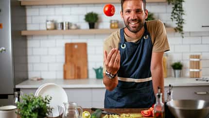 Portrait von einem Mann, der kocht und eine Tomate in die Luft wirft