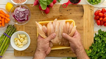 Geflügelfleisch auf einem Holzbrett, Gemüse liegt an der Seite