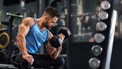 Bodybuilder,Pumping,His,Biceps,With,Dumbbell,In,Gym,,Empty,Space