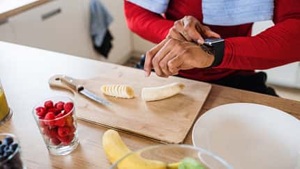 Mann schaut auf seine Fitnessuhr und bereitet Essen zu