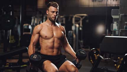 Determined young man lifting up dumbbells in the gym