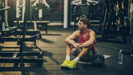 Sportlicher junger Mann sitzt erschöpft auf dem Boden beim Training im Gym