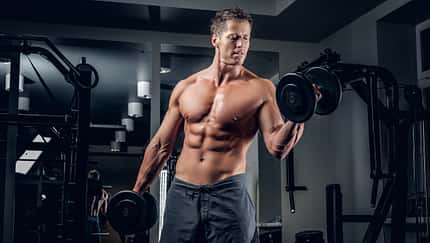 Muscular shirtless male doing biceps exercise with dumbbells.