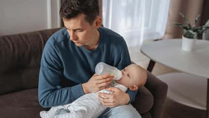 Ein Vater gibt seinem Baby das Fläschchen und schaut deprimiert zur Seite Ein Vater gibt seinem Baby das Fläschchen und schaut deprimiert zur Seite