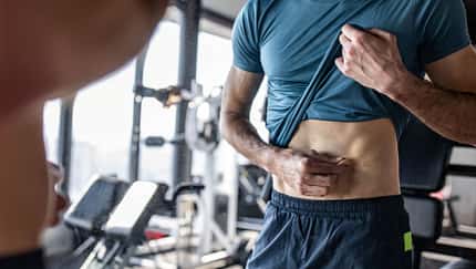 Trainierter, schlanker Mann greift sich in sein Bauchfett Trainierter, schlanker Mann greift sich in sein Bauchfett