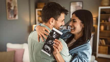 Frau und Mann umarmen sich freudig, sie hält ein Ultraschallbild eines ungeborenen Kindes in der Hand Frau und Mann umarmen sich freudig, sie hält ein Ultraschallbild eines ungeborenen Kindes in der Hand