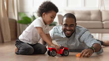 Ein Vater liegt mit seinem kleinen Sohn auf dem Wohnzimmerboden und spielt mit Autos Ein Vater liegt mit seinem kleinen Sohn auf dem Wohnzimmerboden und spielt mit Autos