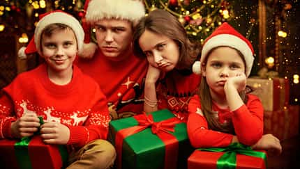 Eine vierköpfige Familie sitzt schlechtgelaunt vor dem Weihnachtsbaum Eine vierköpfige Familie sitzt schlechtgelaunt vor dem Weihnachtsbaum