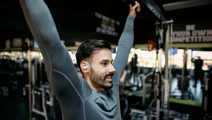 Young sportsman stretching back muscles while listening music in gym
