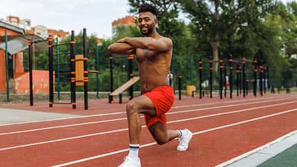 Low angle view of nice young man of Iranian ethnicity with afro hair doing bodyweight walking lunges outdoors