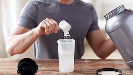 Ein Mann, der sich einen Scoop Kreatin-Pulver in seinen Shaker füllt