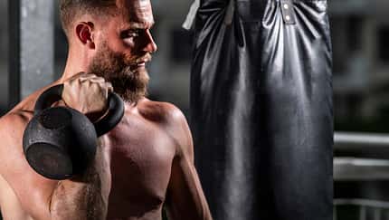boxing bag,colour image,cross fit,fitness,thirties,white man with beard exercising with kettlebell at gym in Bangkok