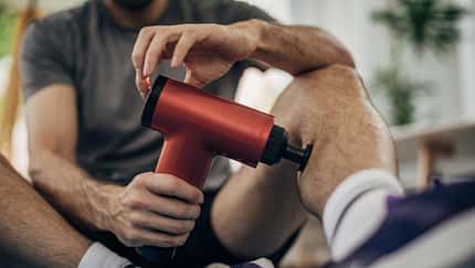 Ein Mann verwendet seine Massagepistole an seinem Bein Ein Mann verwendet seine Massagepistole an seinem Bein