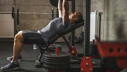 Sports man doing bench press, athlete during training in professional gym, lifting weights for biceps, pectorals and back muscles