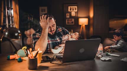 Ein verzweifelter Vater sitzt mit seinem Baby am Rechner