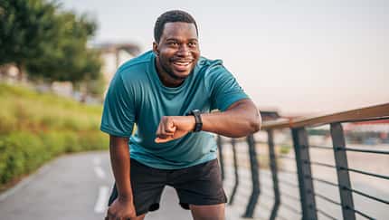 Plus-size black man checking time while jogging outdoors