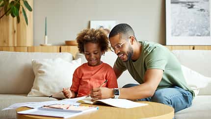Ein Vater sitzt mit seiner Tochter am Wohnzimmertisch und hilft ihr bei den Hausaufgaben Ein Vater sitzt mit seiner Tochter am Wohnzimmertisch und hilft ihr bei den Hausaufgaben