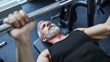 Mann über 40 liegt auf Hantelbank und drückt Gewichte nach oben Mann über 40 liegt auf Hantelbank und drückt Gewichte nach oben