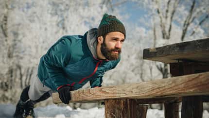 Mann trainiert draußen und macht Liegestütze an einer Holzbank im verschneiten Park. Mann trainiert draußen und macht Liegestütze an einer Holzbank im verschneiten Park.