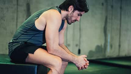 Sportlicher Mann sitzt im Fitnessstudio und schaut erschöpft auf den Boden