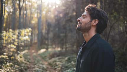 Mann steht im Wald und genießt mit geschlossenen Augen die Ruhe