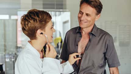 Ärztin untersucht einen Mann mit dem Stethoskop bei einer Vorsorgeuntersuchung. Ärztin untersucht einen Mann mit dem Stethoskop bei einer Vorsorgeuntersuchung.