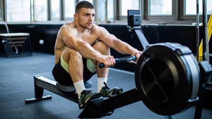 Trainierter Mann sitzt oberkörperfrei auf einem Rudergerät im Fitnessstudio