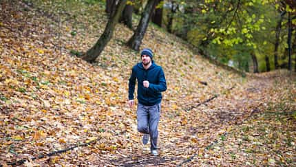Mann läuft im Wald, umgeben von Herbstlaub Mann läuft im Wald, umgeben von Herbstlaub