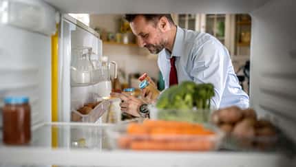 Blick aus dem Kühlschrank: Ein Mann greift nach Lebensmitteln und hält zwei Gläser in der Hand. Blick aus dem Kühlschrank: Ein Mann greift nach Lebensmitteln und hält zwei Gläser in der Hand.
