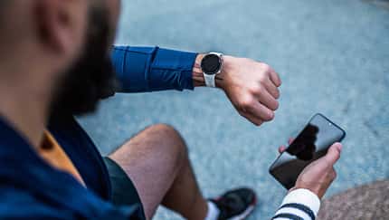 Draufsicht auf einen Mann, der seine Smartwatch prüft und ein Smartphone in der Hand hält.