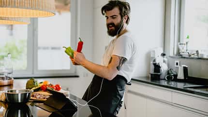 Mann mit Kopfhörern kocht in der Küche und singt mit Paprika in der Hand. Mann mit Kopfhörern kocht in der Küche und singt mit Paprika in der Hand.