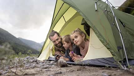 Ein Vater schaut mit seinem kleinen Sohn und seiner kleinen Tochter aus einem Zelt heraus