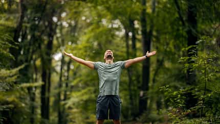 Mann steht im Wald und genießt mit offenen Armen die Natur und spürt Freiheit